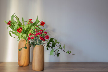 red carnations and tulips in modern vases on background gray wall