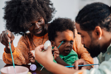 Happy african american parents with toddler son painting easter eggs