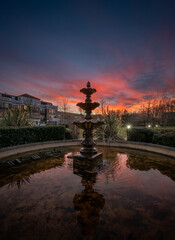 Fountain and pond in a park at sunset with a pink sky. Evening view in portrait orientation with...