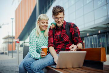 Portrait of friends sitting at campus and looking at the laptop.