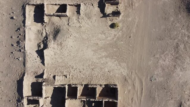 Camera looking down on Delapidated mud brick adobe building in a dry desert landscape with clear blue skies no clouds 