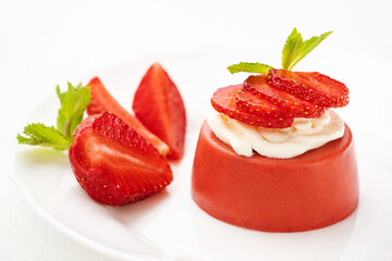 Strawberry mousse or strawberry panna cotta on a plate is decorated with chocolate, ricotta and fresh ripe strawberry slices on a white background. Healthy delicious dessert. Summer time