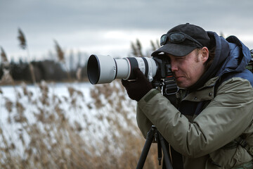 Wildlife photographer is setting up camera on tripod outdoors. Man photographing landscape or...