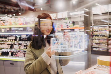 Beautiful woman testing and buying cosmetics in a beauty store. Young girl trying lipstick on hand...