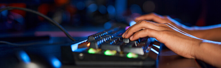 cropped female hands typing on computer keyboard with illumination while playing game, banner