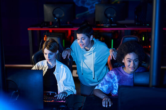 Diverse women engaged in cybersport games, using computers and smiling in room with blue light