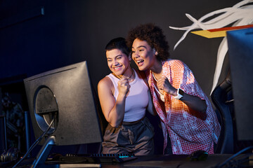 two interracial and happy women celebrating victory after winning in gaming room, cybersport