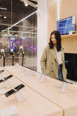 Korean teenage girl choosing phone at technology store. Female customer viewing smart phones in...