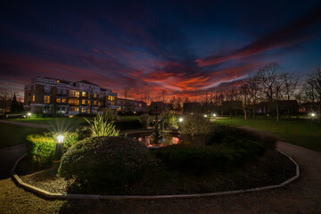 Fountain and pond in a park at sunset with a red sky. Wide angle night view in landscape...