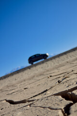 desert landscape with cracked soil with car out of focus on ascending path.