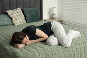 Sad young woman lying on bed at home