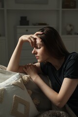 Sad young woman sitting on sofa at home