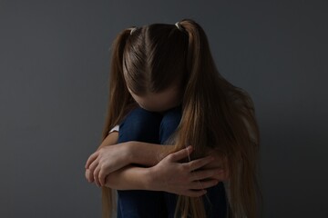 Sad girl sitting near dark grey background
