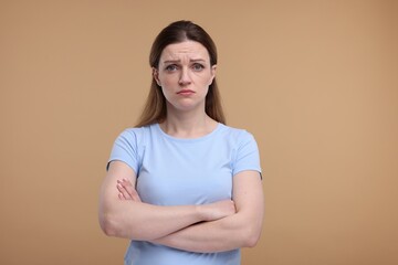 Obraz premium Portrait of sad woman with crossed arms on beige background