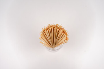many small toothpicks or wooden skewers lie in a glass with a white background