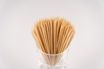 many small toothpicks or wooden skewers lie in a glass with a white background