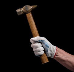 A man's hand in a white work glove holds a used metal hammer with a wooden handle on a black...