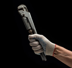 A man's hand in a white work glove holds an old gray gas pipe wrench on a black background.