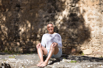 Non-binary person, young and South American, heavily makeup and sitting on a stone, looking at the...