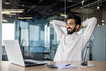Relaxed indian businessman with beard enjoying break at modern office desk