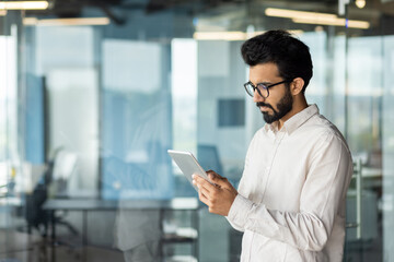 Focused indian businessman with beard using tablet in modern office space