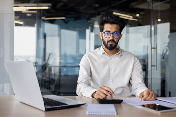Fototapeta na wymiar Focused indian businessman working on laptop in modern office space