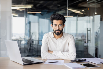 Fototapeta na wymiar Confident indian businessman with beard working at desk in modern office