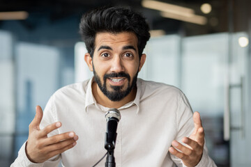Confident indian businessman giving a speech with microphone in office setting