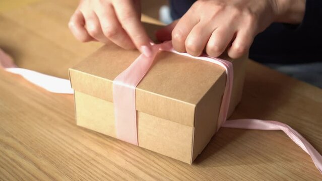 Close-up of woman's hands opening a gift with a pink ribbon. Give gifts. The buyer looks at his order. Purchasing skincare products	