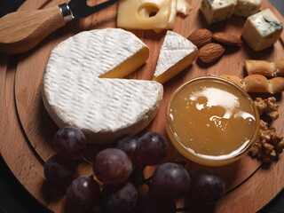 Sliced Brie cheese served with knife, honey, nuts and grape on wooden board