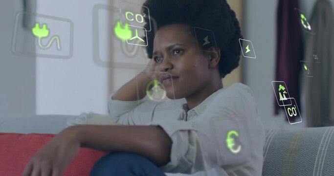 Animation of ecology icons over happy african american woman relaxing at home