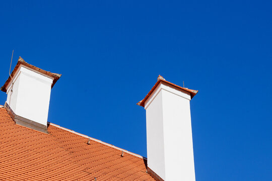 white chimney on a tiled roof in front of a bright blue sky
