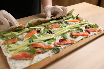 Lavash with filling is wrapped in a roll. Preparation of a roll with cheese, fish and vegetables