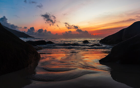 Seaside landscape photo with wet sand and coastal stones on the sunset