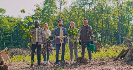 Portrait of beautiful caring active group of people standing in forest before forestation holding...