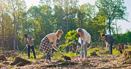Side-view of charming middle-aged Caucasian woman holding and planting trees with beautiful young...