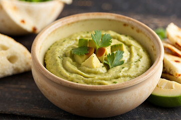 Avocado hummus in rustic bowl with pita wedges around