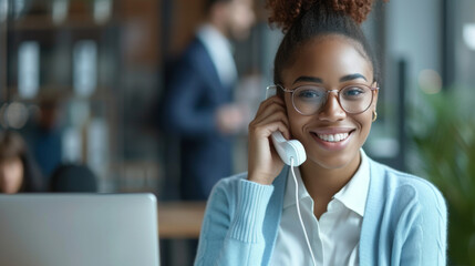 A smiling woman in an office is happily speaking on a telephone, likely engaging in a cheerful customer service conversation. - obrazy, fototapety, plakaty