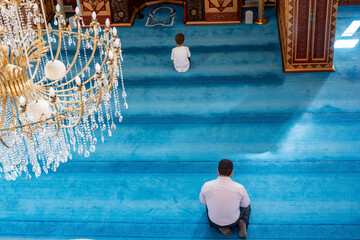 Adult and child are praying inside mosque  with blue carpet