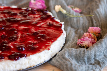 Cold cheesecake with cherry jelly and roses around it served on wooden background with green throw and antique forks