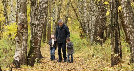 Man running around autumn forest holding hands of two sons 