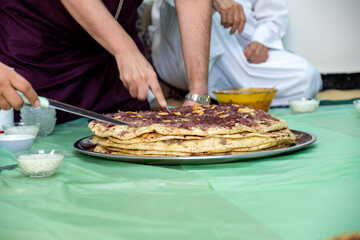 Man hands cutting musakhan bread with knife for guests and family to eat together