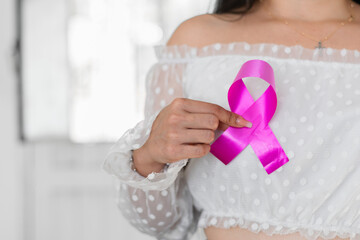 latina woman holding a pink ribbon in her hand as she puts it on her breast, fighting breast cancer