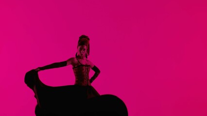 Woman dancer dancing on pink background. Female in flamenco style dress performs elegant spanish dance moves with her hands and body in the studio.