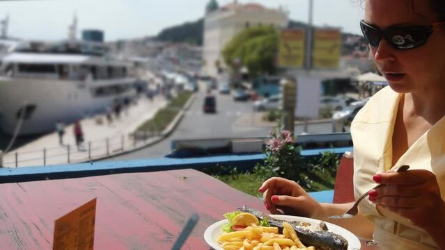 Woman in sunglasses eat fish in restaurant on sunny day