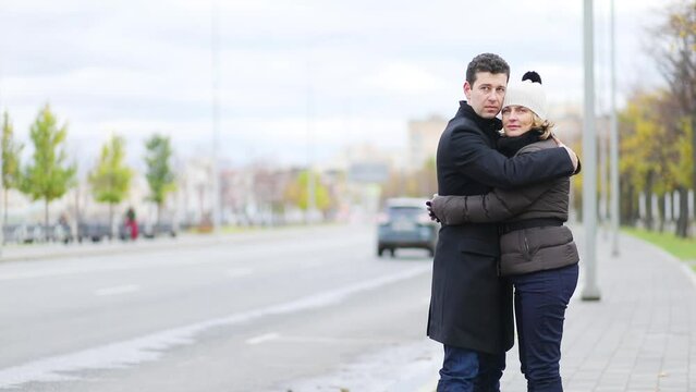 Happy man and pretty woman stands and hug near city road at autumn day, shallow dof