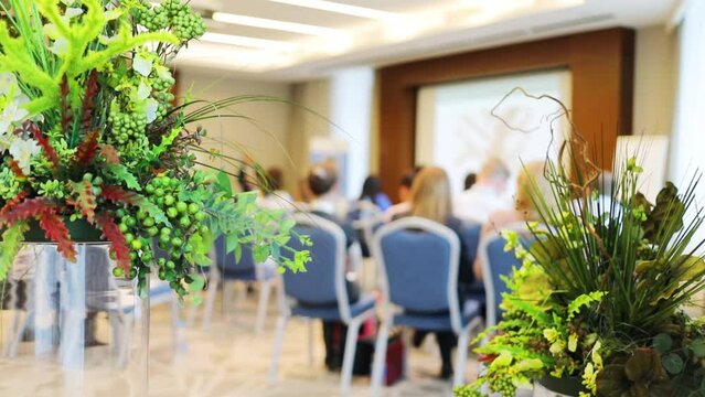 Back of audience during conference, focus on decorative plants