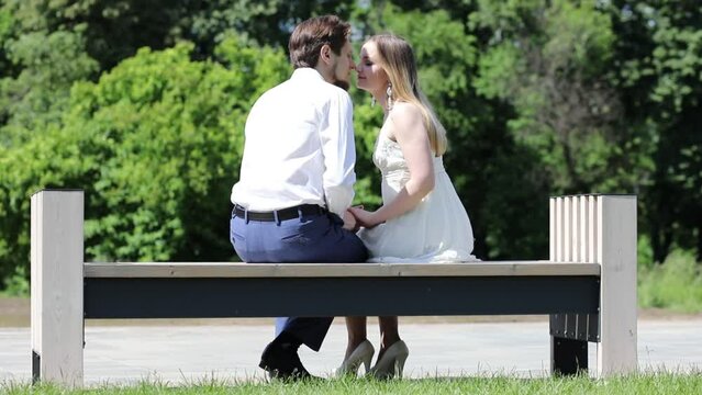 Woman and man sits on bench in park with lilac at sunny day, slow motion