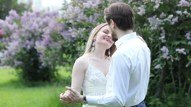 Woman and man dance in park with lilac at sunny day, slow motion