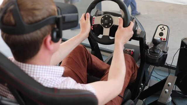 Boy plays auto simulator with rudder and head display, back view, slow motion